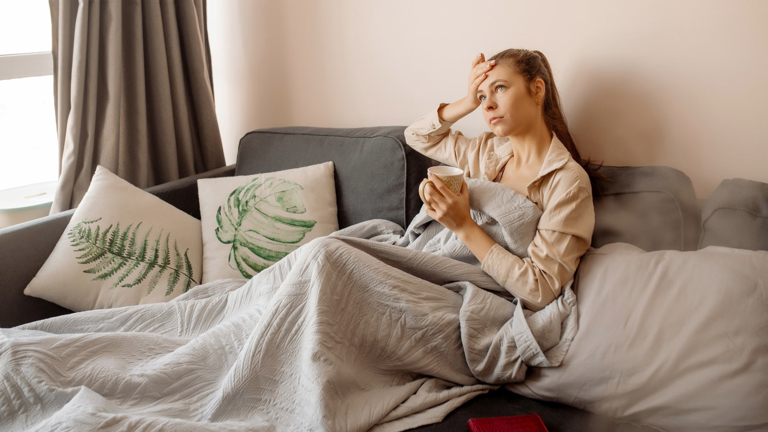 Frau liegt krank mit einer Tasse auf der Sofa