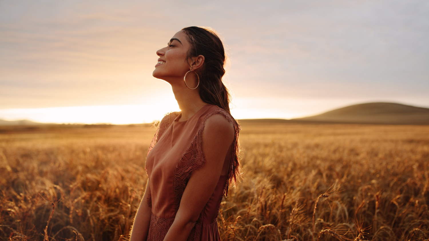 Lächelnde Frau steht im Weizenfeld bei Sonnenuntergang